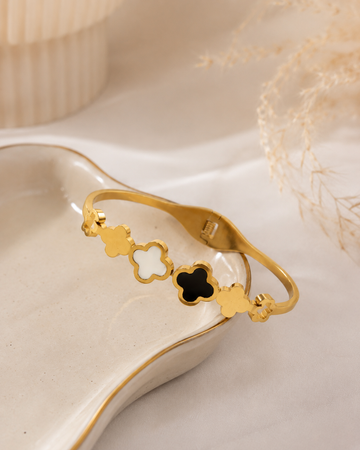 Gold clover bangle bracelet with black and white enamel on ceramic dish – side angle view