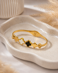 Gold clover bangle bracelet with black and white enamel on ceramic tray – top view