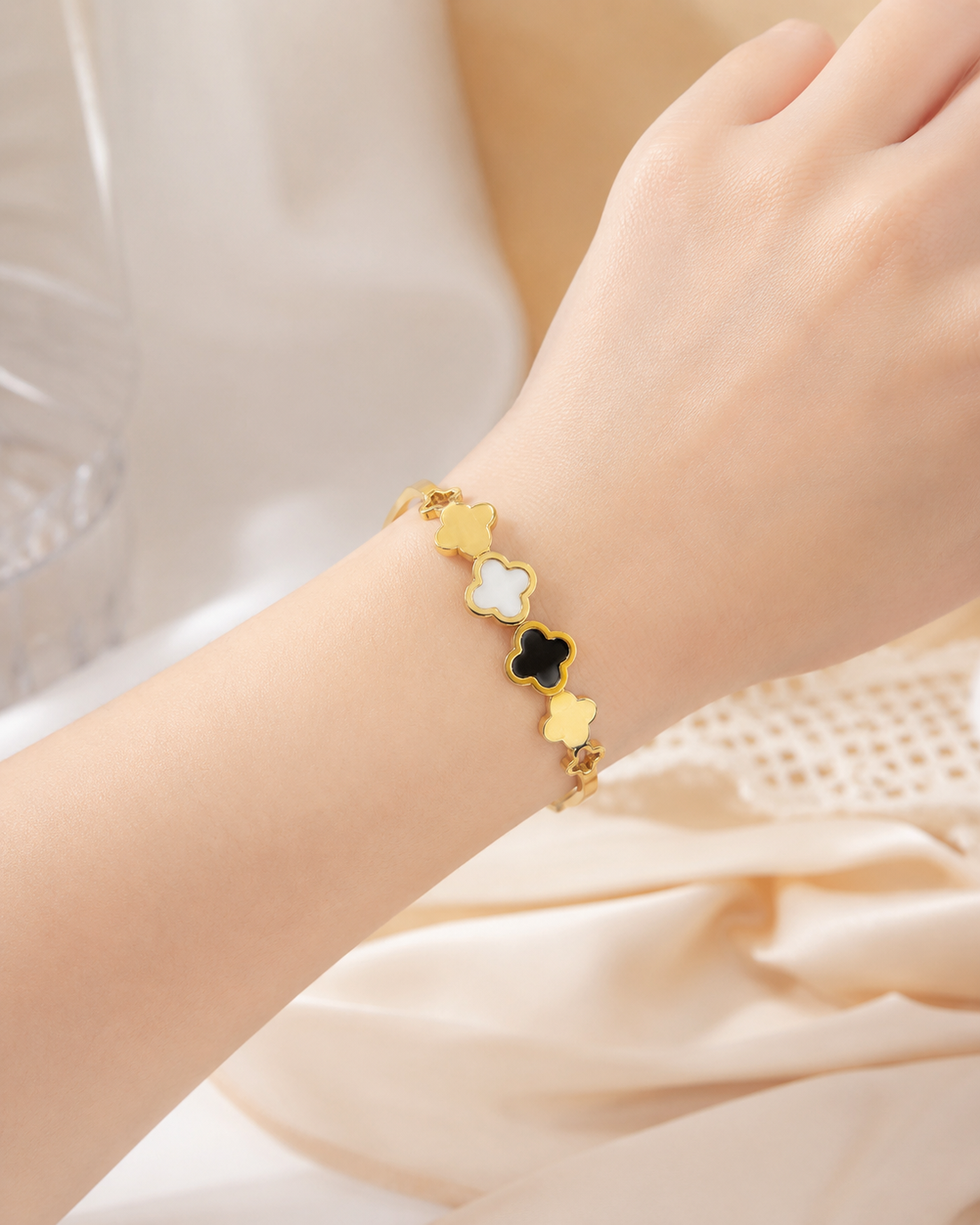 Gold clover bangle bracelet with black and white enamel on ceramic dish – side angle view